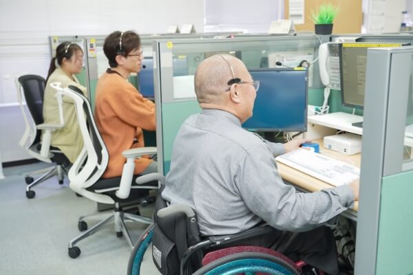 車椅子を使用している社員がオフィスでコンピュータに向かって作業している様子