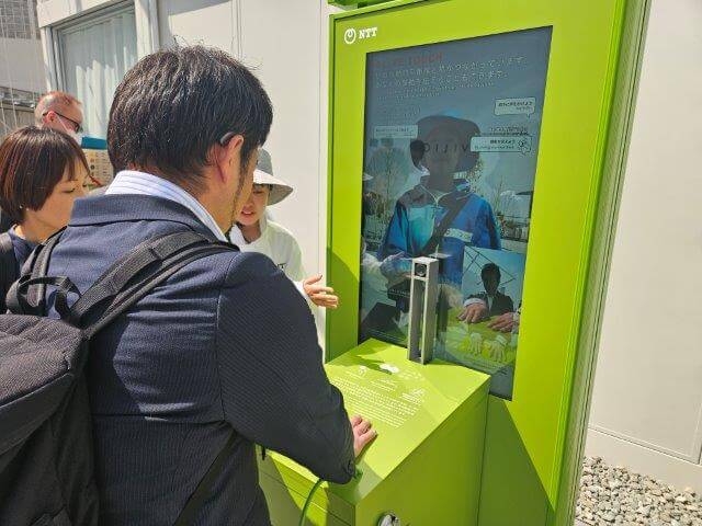 画像:屋外で聴覚障がい者の社員が「触れ合う伝話」を体験中の様子