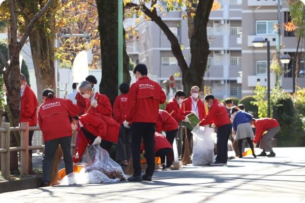 写真：赤いジャケットを着た大勢のNTTクラルティ社員による職場周辺の清掃活動
